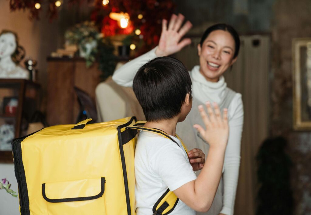 Parent waving goodbye at nursery door, child waving back.